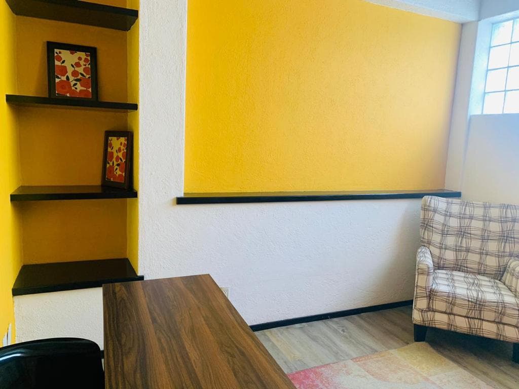 Oficina privada con pared amarilla, repisas y sillón