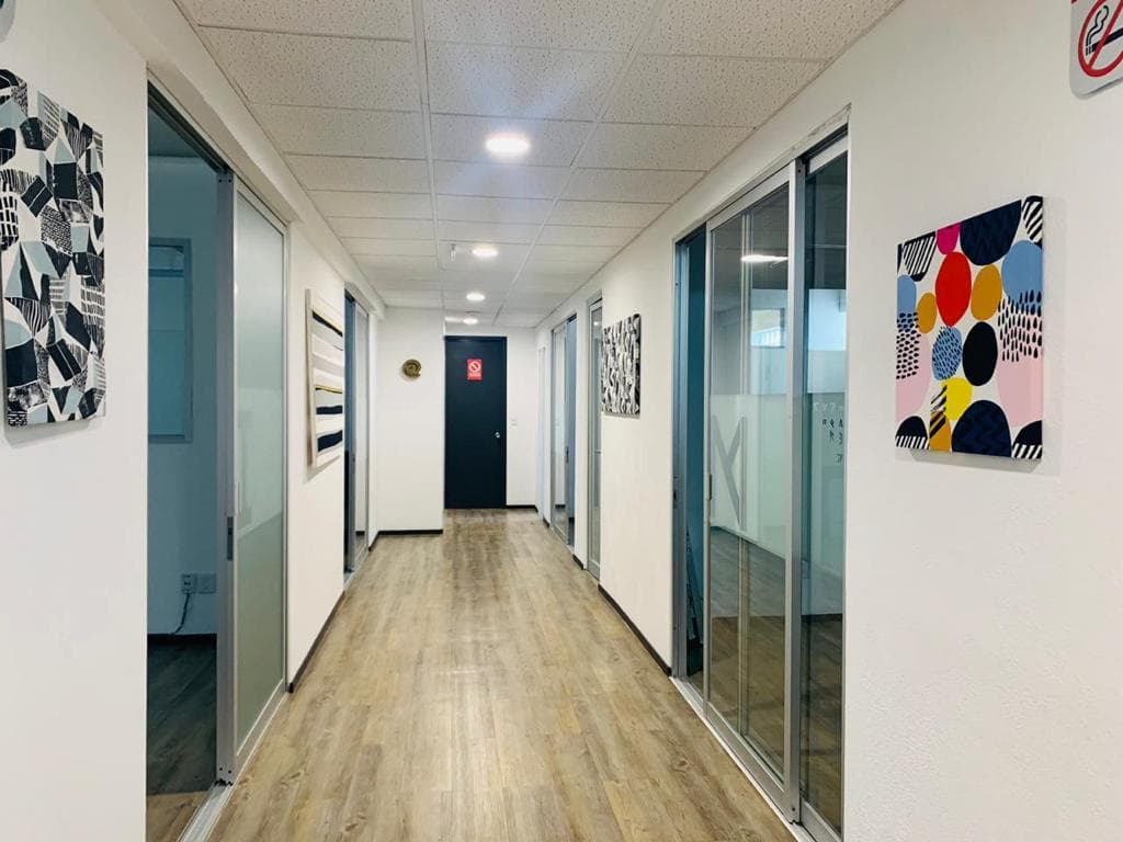 Pasillo de oficinas privadas con puertas de cristal y cuadros