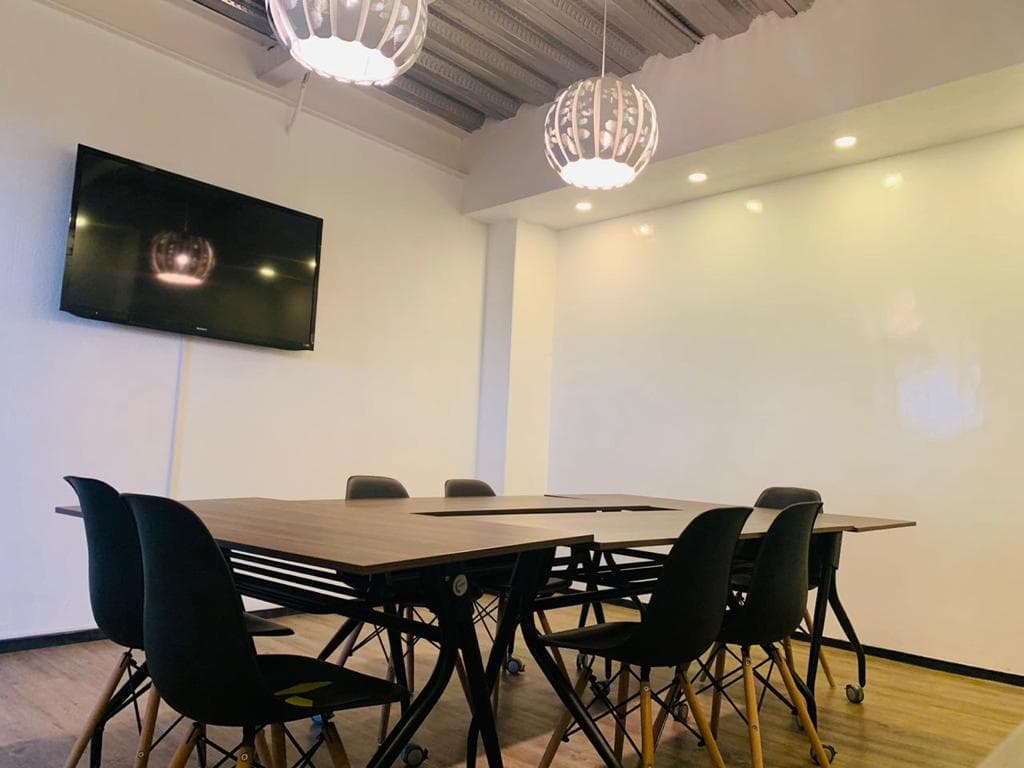 Sala de juntas con mesa modular, pantalla y muro pizarrón