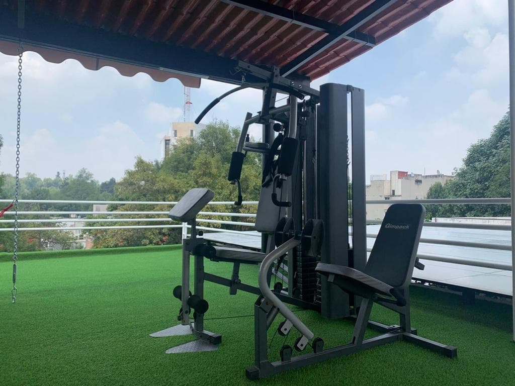Gimnasio con equipo multifuncional sobre pasto sintético en la terraza